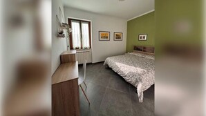 Ein Schlafzimmer mit einem Bett, einem Schreibtisch, einem Stuhl, einem Heizkörper und zwei Fenstern mit Vorhängen.