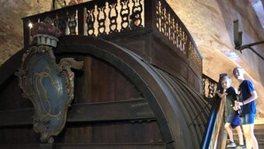 A large wooden barrel-like structure with a decorative metal plaque, a staircase with a railing, and a stone wall. - Charming studio with AC, balcony and view of the Castle - Walk to Everything. (Heidelberg)