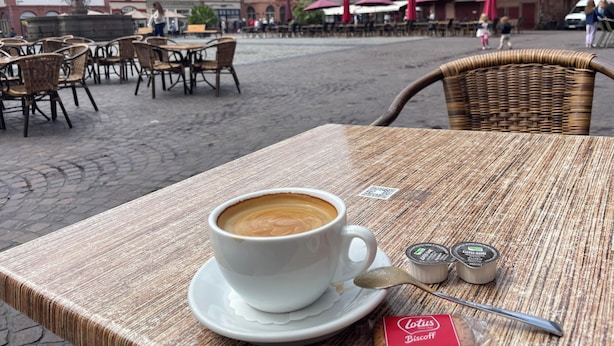 A table with a cup of coffee, a spoon, and a packet of coffee creamer. - Charming studio with AC, balcony and view of the Castle - Walk to Everything. (Heidelberg)
