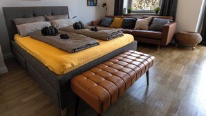 A modern bedroom with a large bed, a bench, a sofa, and two abstract paintings on the wall. - Charming studio with AC, balcony and view of the Castle - Walk to Everything. (Heidelberg)