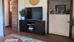 Una sala de estar con un televisor de pantalla plana sobre un soporte de madera oscura, un tapiz de pared tejido y una estación de café con un letrero que dice 