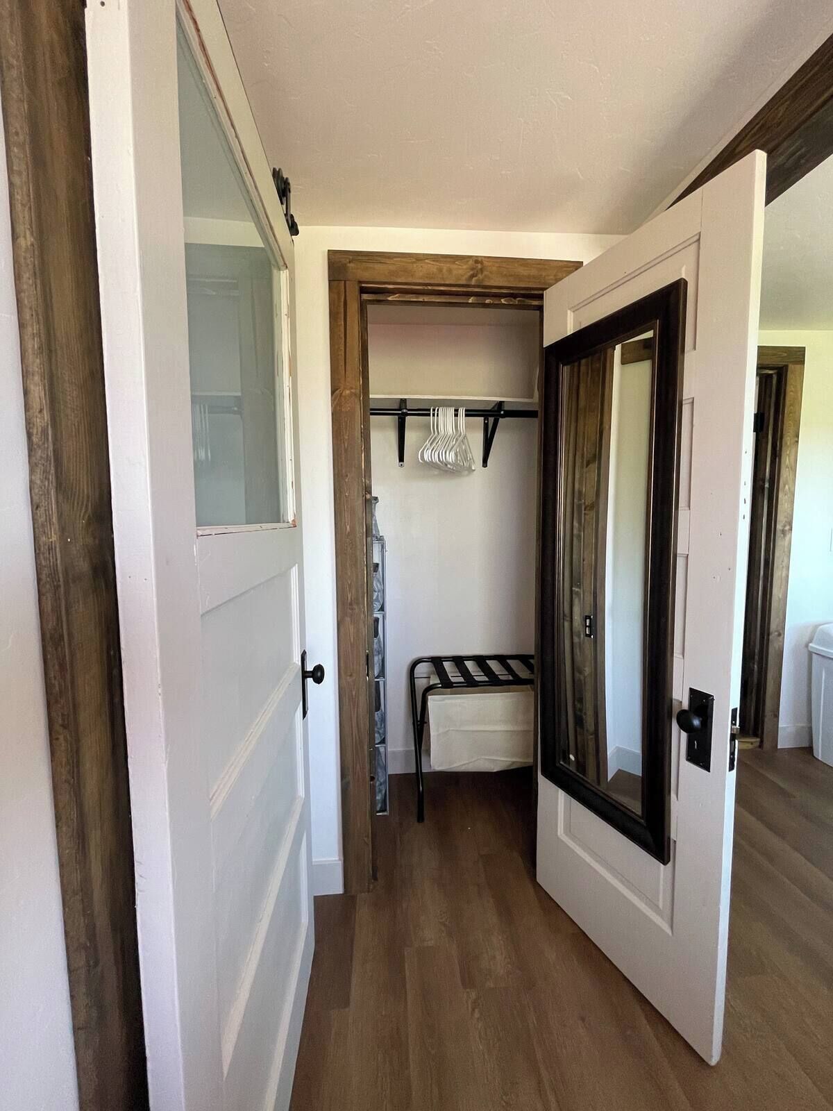 A hallway with a wooden floor, a white door with a black frame, and a small bed with a white sheet.