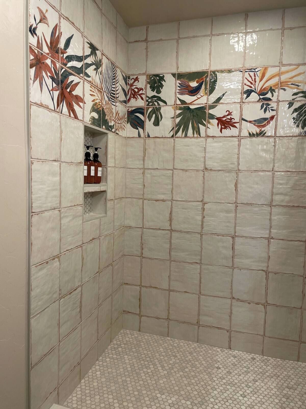 A bathroom with tiled walls, a shower area, and a shelf with toiletries.