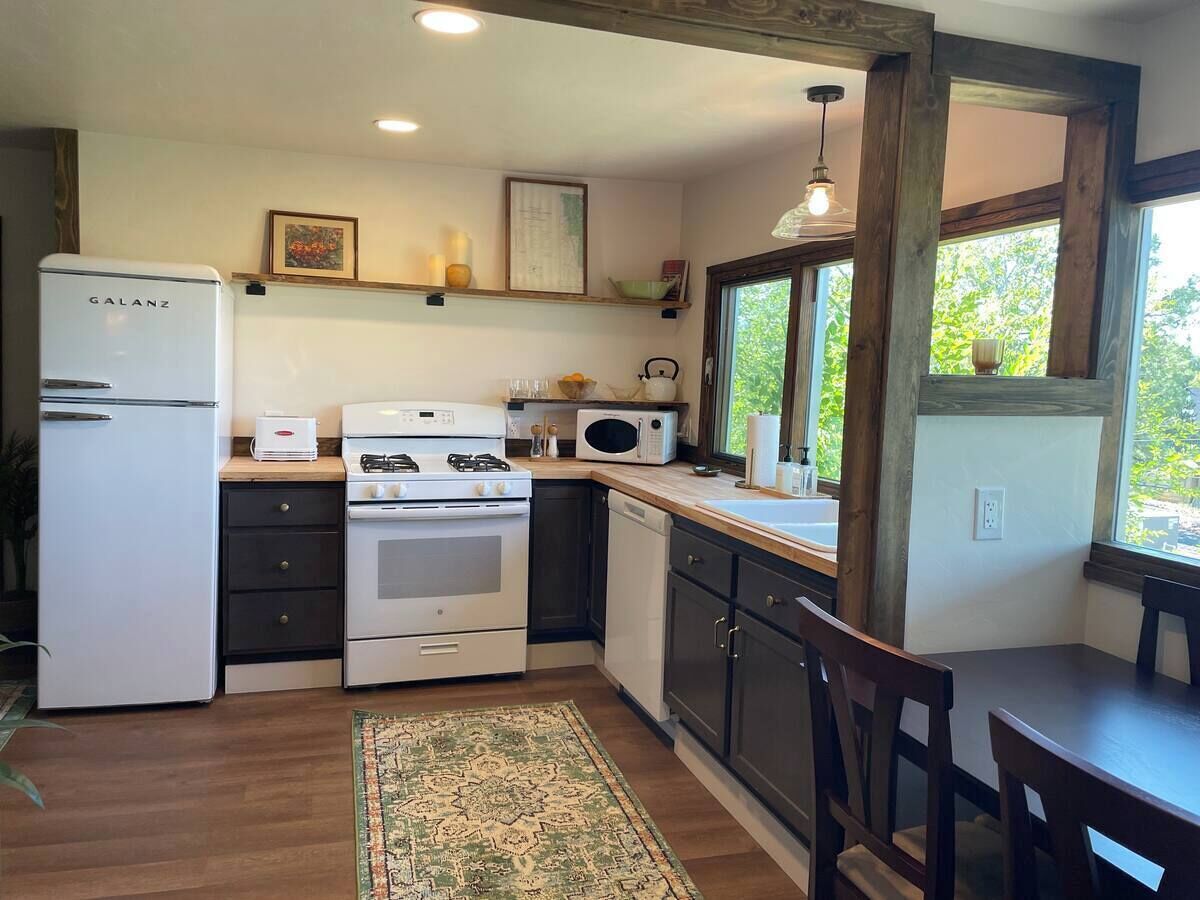 Una cocina funcional con refrigerador, estufa, microondas y lavaplatos. Una ventana proporciona luz natural y vistas al exterior.
