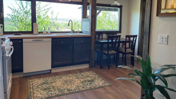 Una cocina con armarios oscuros, un lavavajillas blanco y una ventana con vistas a zonas verdes.