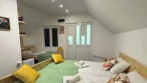Een slaapkamer met twee bedden, elk voorzien van een groen-witte dekbedovertrek, gele en bloemenkussens, en netjes opgevouwen witte handdoeken.