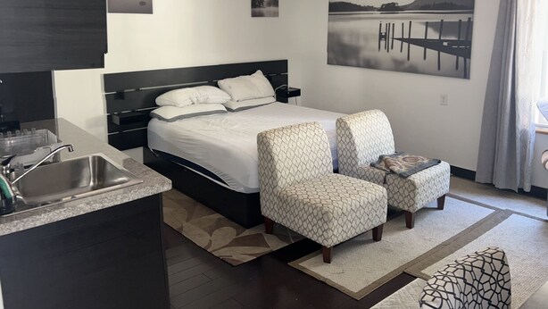Ein modernes Hotelzimmer mit einem Bett, zwei Sesseln, einem kleinen Tisch, einem Waschbecken und einem Gemälde eines Sees.