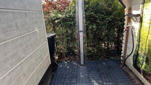 A small outdoor area with a wooden deck, a metal water feature, and a garden with trees and shrubs.