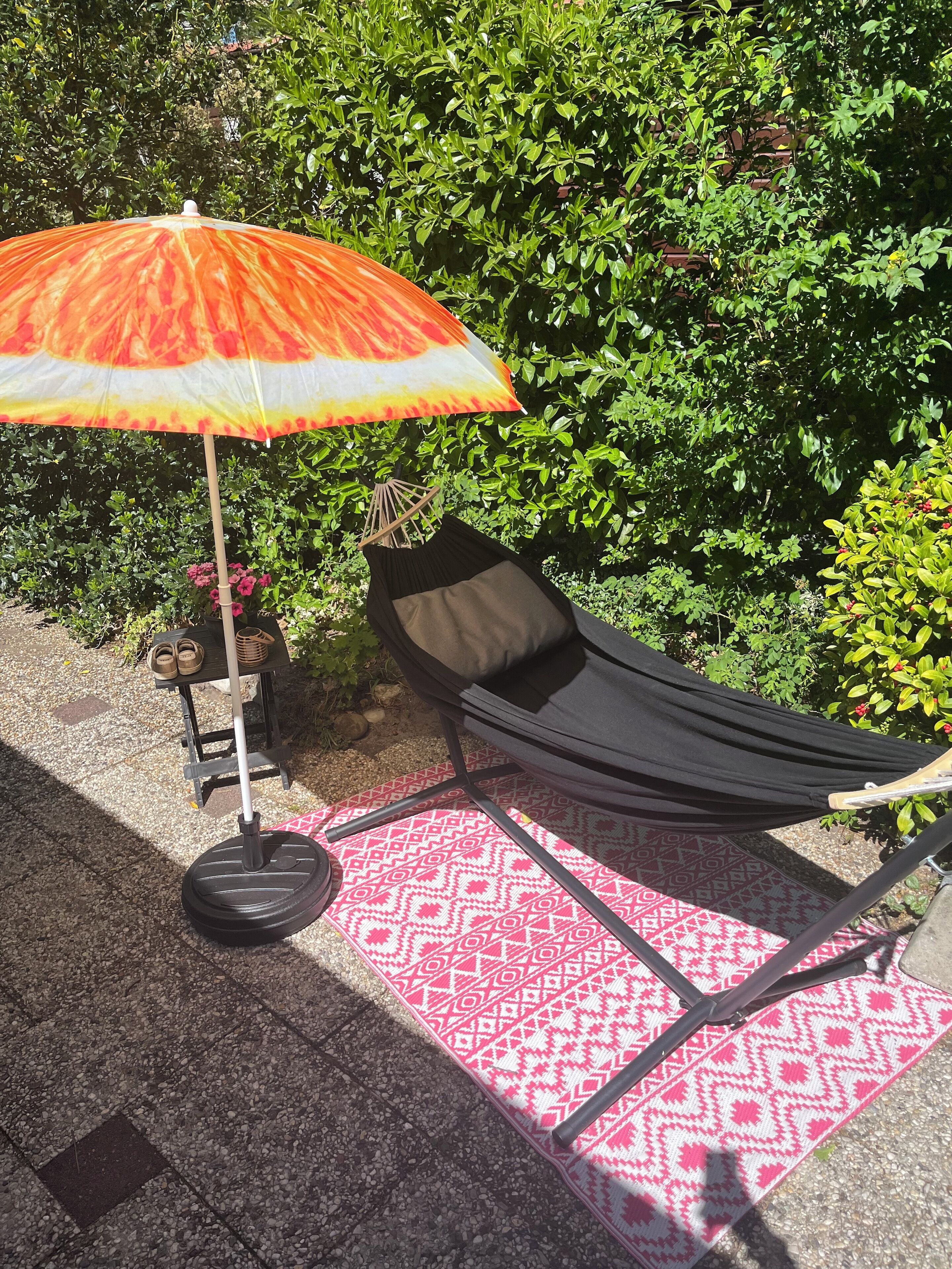 A hammock chair with a black cushion, a patterned rug, and an umbrella.