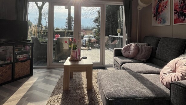 A living room with a sofa, a coffee table, and a TV. There is a large window with a view of the outside.