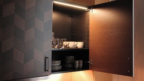 Une cuisine avec un meuble en bois contenant de la vaisselle, des verres et un four à micro-ondes.