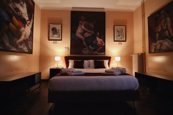 A hotel room with a large bed, two bedside tables with lamps, and three framed artworks on the walls.