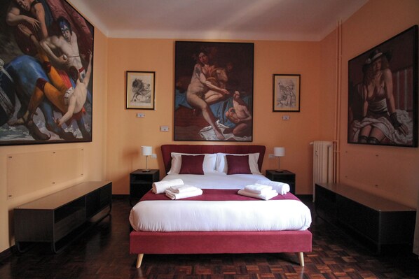 Un letto grande con lenzuola bianche e rosse, due comodini con lampade e opere d'arte alle pareti.