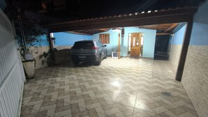 A covered parking area with a tiled floor, a parked car, and a building entrance. - Beach retreat (São Sebastião)