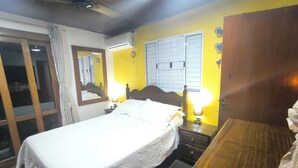 A bedroom with a bed, bedside tables, a mirror, and a window with blinds. - Beach retreat (São Sebastião)