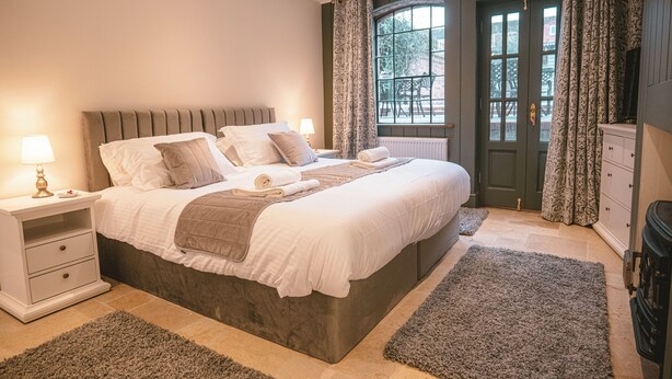 Un dormitorio con una cama grande, mesitas de noche, un aparador y una ventana con cortinas.