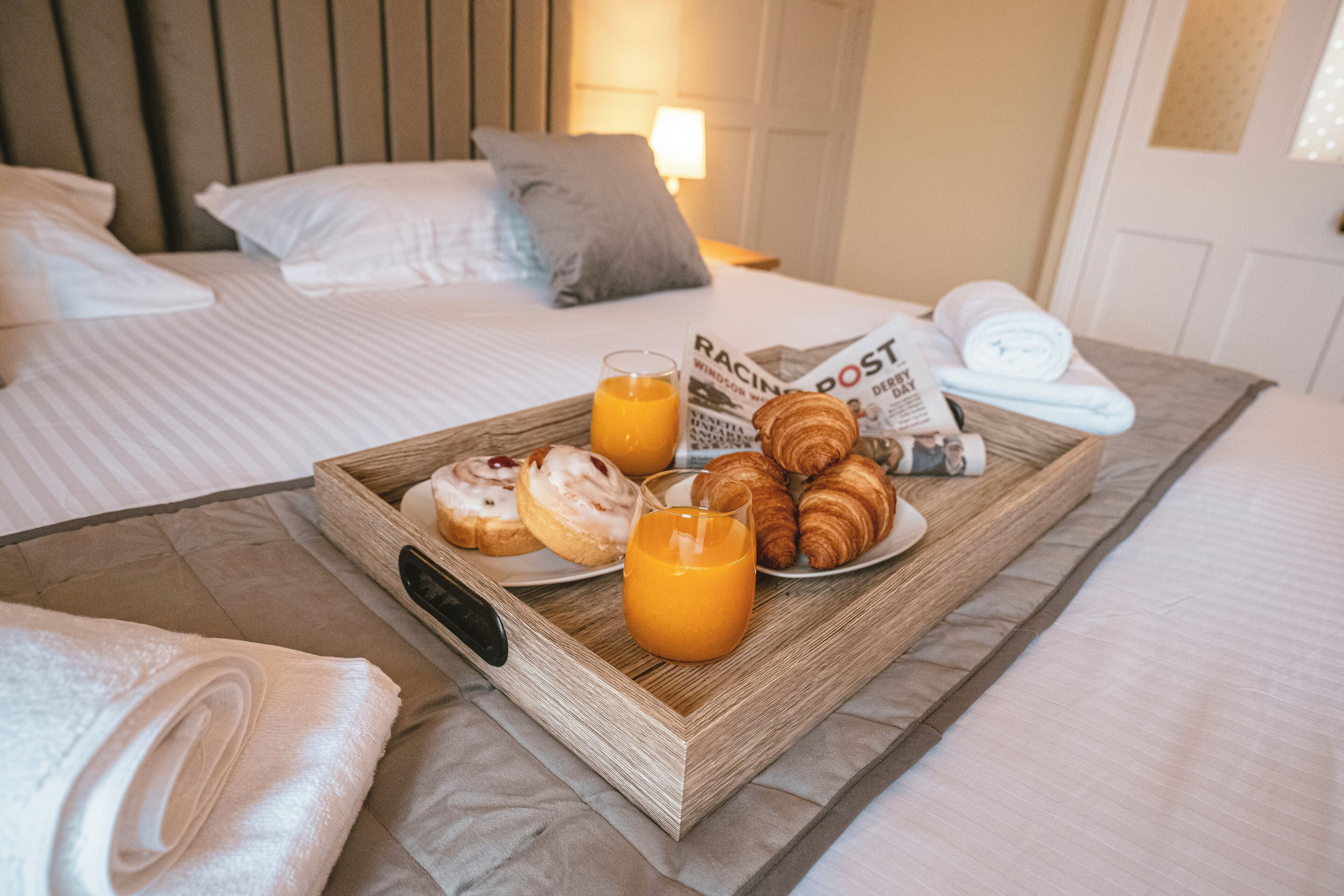 A neatly made bed with a tray of breakfast items including croissants, muffins, and orange juice, along with a newspaper.