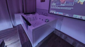 Une salle de bain moderne dotée d’une grande baignoire, d’un espace douche et d’un écran mural sur lequel est diffusé un film.