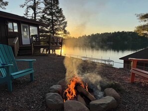 A lakeside cabin with a fire pit, outdoor seating, and a view of the lake. - Renovated 6BR Waterfront Lodge on Round Lake | Private Dock & Sandy Shore (Hayward)