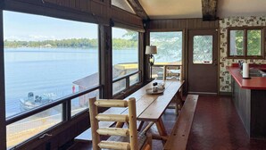 A dining area with large windows overlooking a lake, wooden furniture, and a kitchen area with a red countertop.