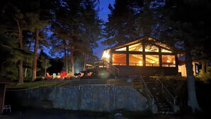A modern house with a glass facade, surrounded by trees, and featuring a stone wall and outdoor seating area.