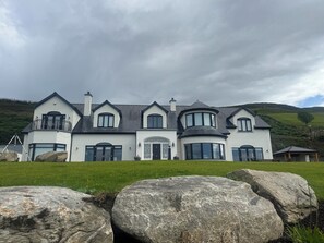 A large, modern house with a symmetrical design, featuring multiple windows and a prominent entrance.