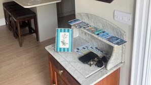 Une salle de bain avec un comptoir en marbre, un meuble-lavabo en bois, un miroir et une petite étagère avec des magazines et un téléphone.