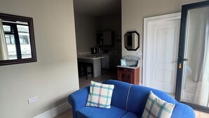 Un salon avec un canapé bleu, un coussin décoratif à motifs, un miroir et une porte donnant sur la cuisine.