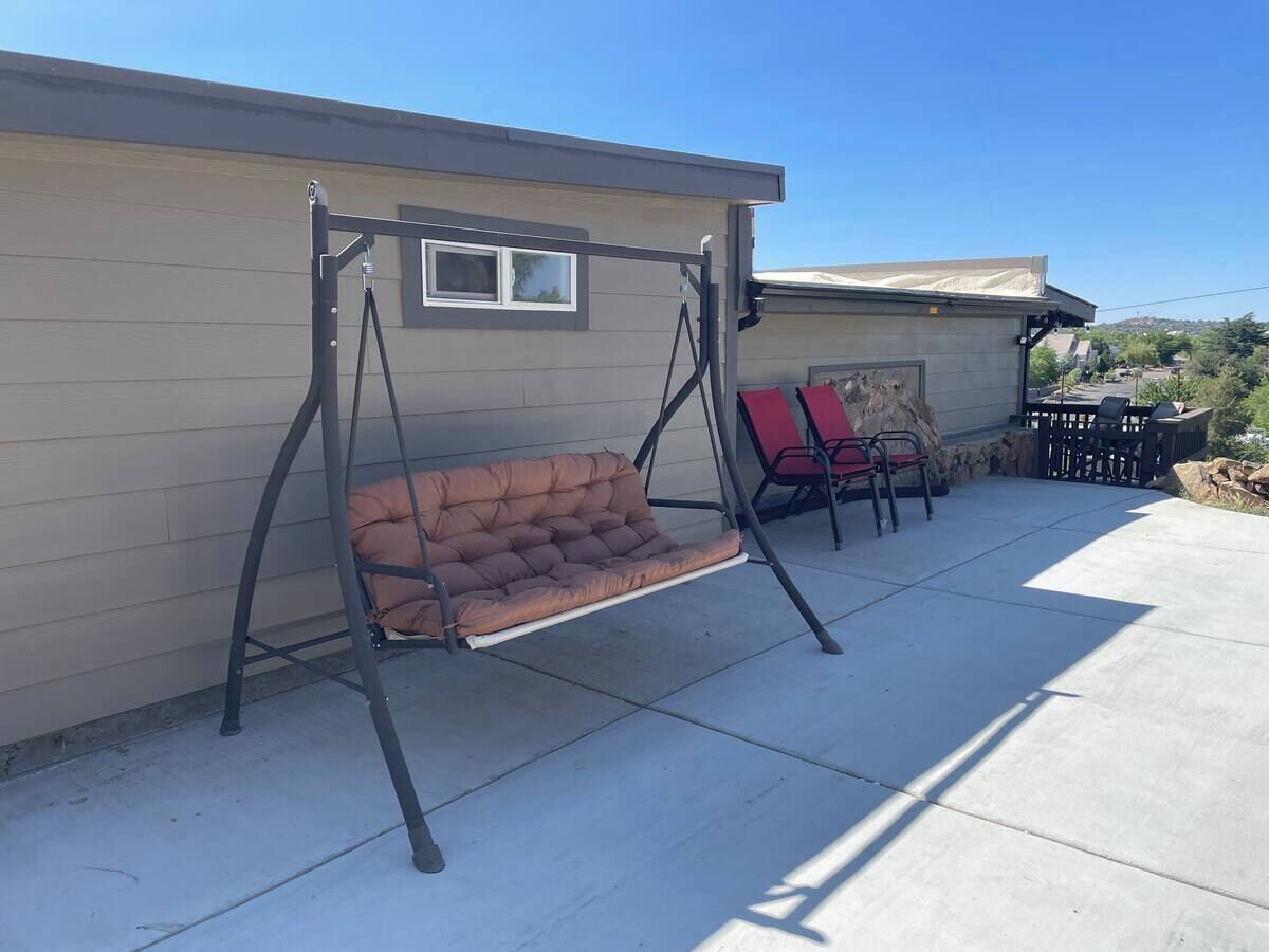 Een terras met een hangstoel, een rode stoel en een tafel.