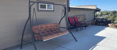Een terras met een hangstoel, een rode stoel en een tafel.