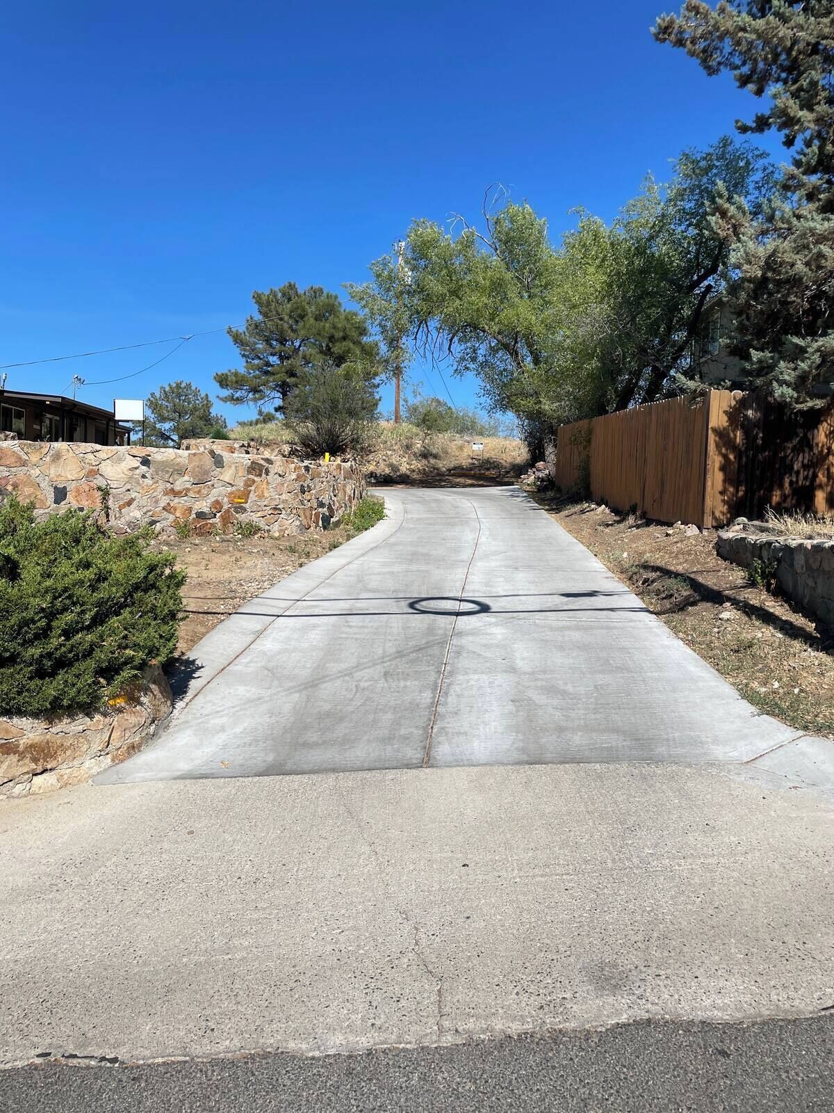 A paved driveway leading to a house with a stone wall on one side and a wooden fence on the other.