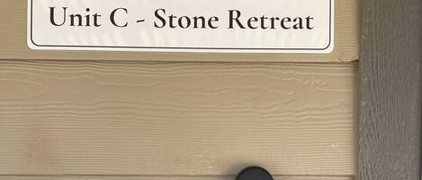 A door with a sign reading 'Unit C - Stone Retreat' and a black security device on the door.