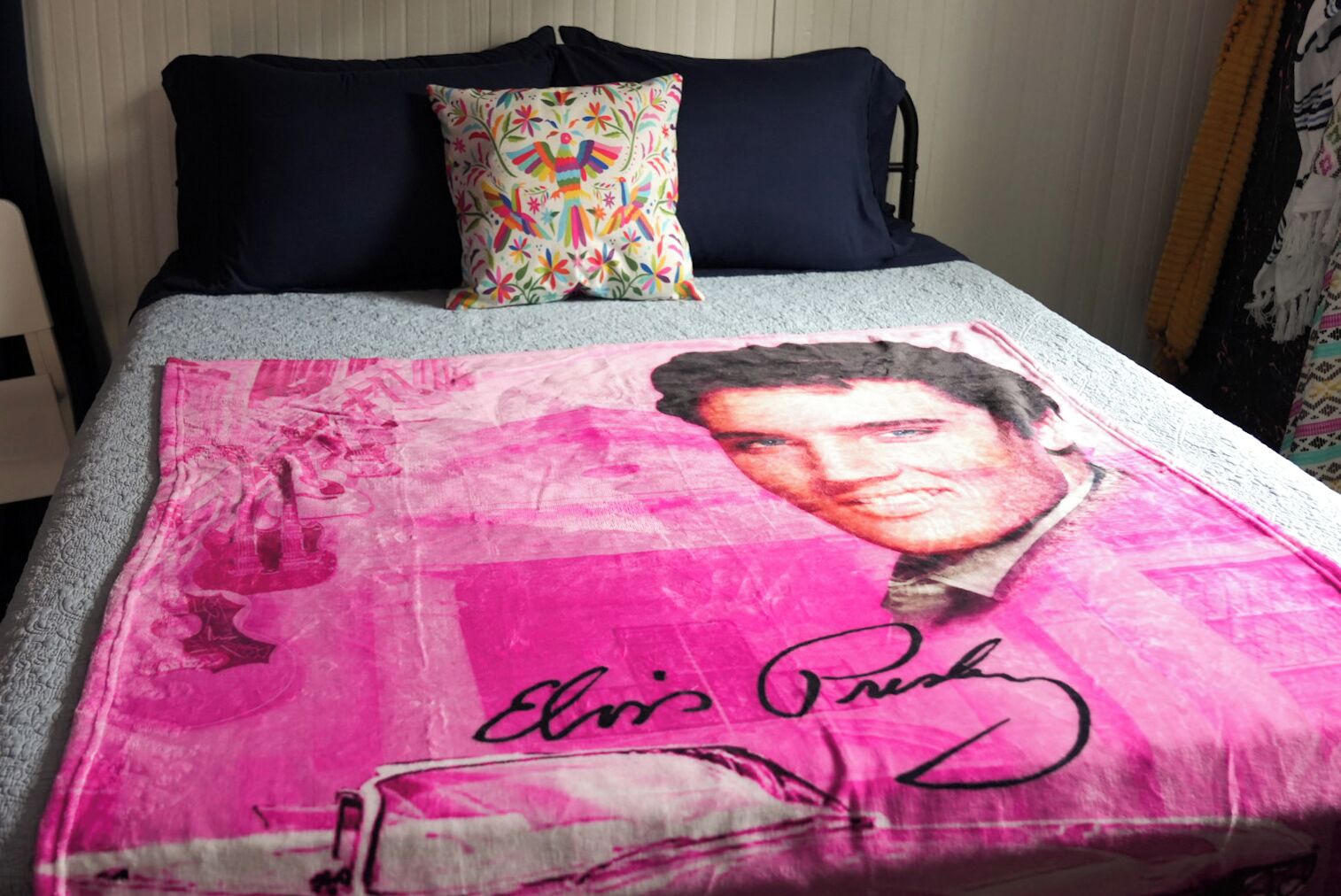 A bed with a colorful pillow and a blanket featuring a celebrity's portrait and signature.
