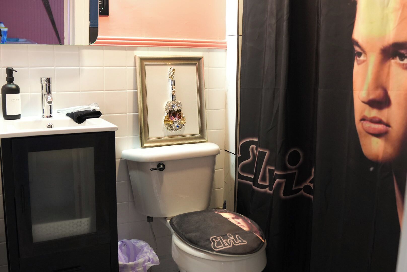 A bathroom with a toilet, a framed picture on the wall, a sink with toiletries, and a shower curtain with a graphic.