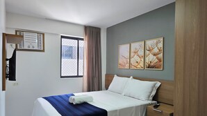 Een hotelkamer met een bed, een raam, een wandgemonteerde airconditioning en een serie van drie ingelijste foto's.