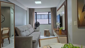 Een moderne woonkamer met een bank, een eettafel met stoelen, een televisie en een ventilator.