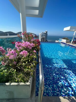 A pool with blue mosaic tiles, surrounded by pink flowers, and overlooking a cityscape with a clear sky. - Style and comfort by the Caribbean (Gaira)