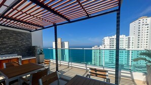 A balcony with a wooden table and chairs, a stone wall, and a view of high-rise buildings and the ocean. - Style and comfort by the Caribbean (Gaira)