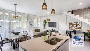 A modern kitchen with a central island, a dining area with a glass table, and a staircase leading to an upper level.