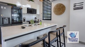 A modern kitchen with a central island, bar stools, and a kitchen sign.