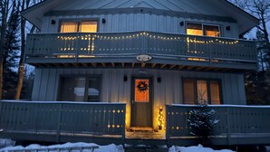 A two-story house with a balcony, a welcome wreath, and a sign indicating it is a ski resort.