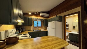 A kitchen with wooden cabinets, a stove, a refrigerator, and a window with curtains. - Powdery Peak Ski Chalet- Where Mountain Memories Begin (Bessemer)