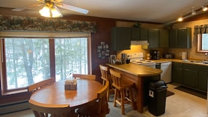 A kitchen with a dining area, wooden furniture, a ceiling fan, and a view of trees outside.