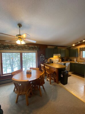 A kitchen with a dining area, wooden furniture, a ceiling fan, and a view of trees outside. - Powdery Peak Ski Chalet- Where Mountain Memories Begin (Bessemer)
