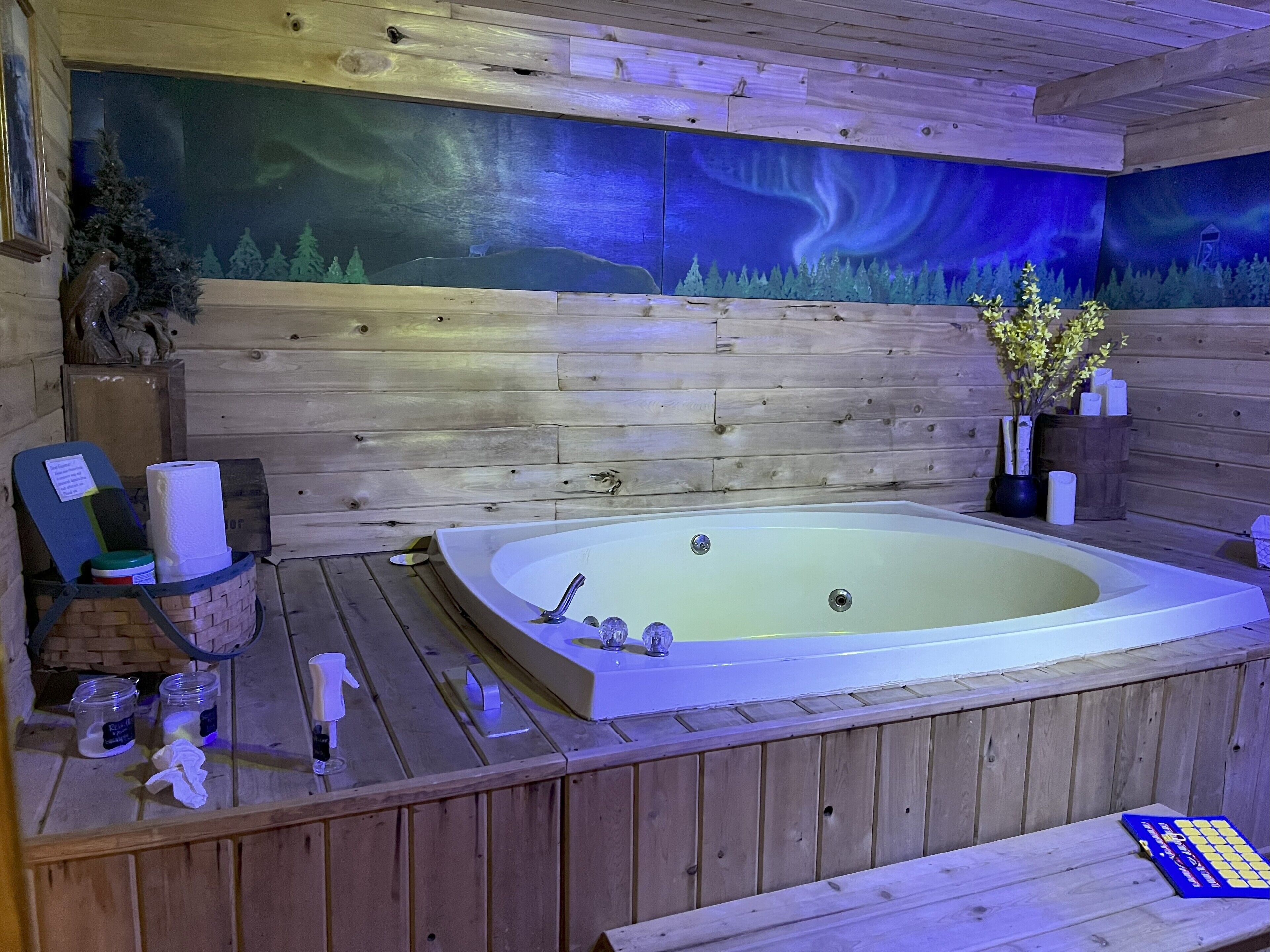 L’intérieur d’un chalet en bois, avec une grande baignoire, des murs en bois et une fresque représentant une scène de forêt.