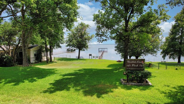 A grassy area with a sign for Northlake Estates Park, a dock, and a building in the background.