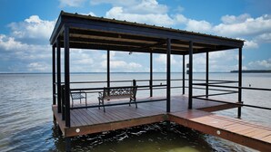 A wooden dock with a metal railing and a bench, extending into a calm body of water.