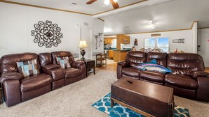 A spacious living room with leather sofas, a coffee table, and a ceiling fan.