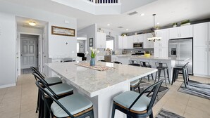 A modern kitchen with a large island, white cabinetry, stainless steel appliances, and a chandelier. - Emerald Island Resort 6 Bed Pool & Spa-10min to Disney! (Kissimmee)