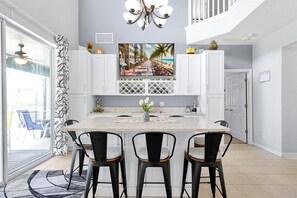 Una cocina moderna con una isla central, armarios blancos y un ventanal con vistas a la playa.